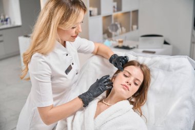 Avrupalı kadın güzellik uzmanı, bulanık güzellik salonundaki kanepede güzel beyaz kadın şırıngası ile güzellik aşısı yaptırıyor. Yüz bakımı, kaldırma ve gençleştirme