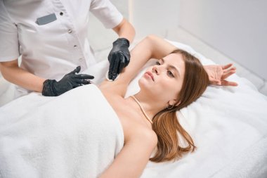 Kesilmiş kadın güzellik uzmanı, bulanık güzellik salonundaki kanepede genç, beyaz kadın şırıngası ile koltuk altı güzellik iğnesi yapıyor. Vücut bakımı, kaldırma ve gençleştirme