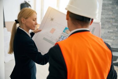 Şen şakrak iş kadını ve teknik mühendis bina planına bakarken odada duruyor ve yenilemeyi tartışıyorlar.