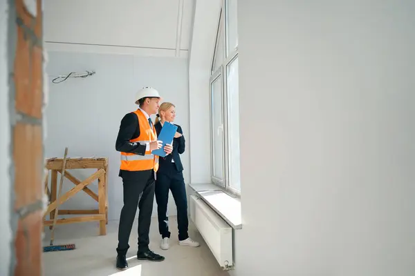 Lächelnder Bauingenieur Hält Klemmbrett Der Hand Während Mit Arbeitgeberin Fenster — Stockfoto