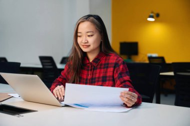 Genç, konsantre Asyalı kadın bilişim çalışanı, birlikte çalıştığımız ofiste dizüstü bilgisayar izliyor. Modern serbest çalışma kavramı veya uzak çalışma