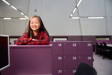 Genç gülen Asyalı bayan bilişim çalışanı ortak çalışma odasındaki dolapta duran kameraya bakıyor. Modern serbest çalışma kavramı veya uzak çalışma