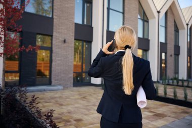 Kadın mimarın arka plan fotoğrafı. Evlerin önünde durmuş telefonla konuşurken ve sarılı planı tutarken.