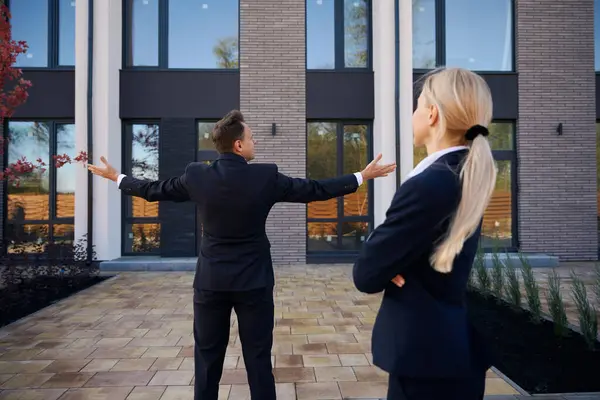 不動産エージェントは 女性のクライアントに新しい家を示すときに彼の腕を横に置いている間立っています — ストック写真