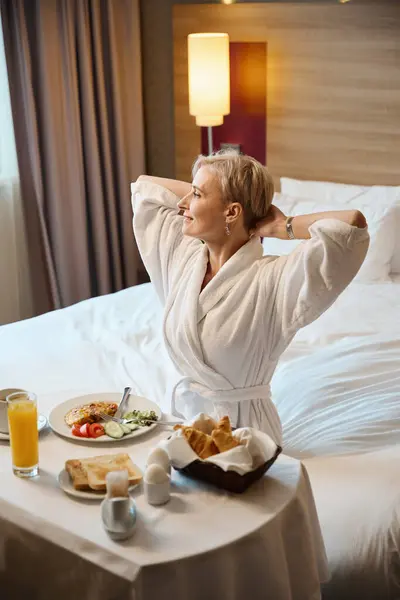 Smiling adult caucasian woman looking away after having breakfast in hotel room at morning. Concept of rest, vacation and travelling