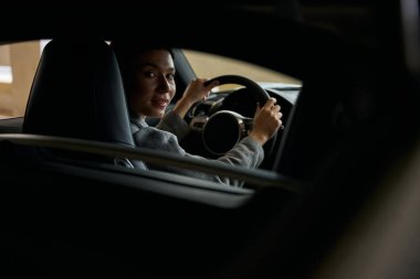 Kadın, kameraya bakarken kontrol ve güvenlik için direksiyonu tutuyor. Arabanın iç görünümü.