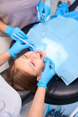 Girl in the dentists chair, medical staff uses special tools at work clipart