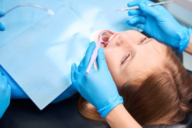 Doktor dişleri ve tartarı temizlemek için özel aletler kullanır. Kız ağzı açık oturur.