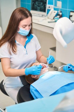 Rahat bir dişçi koltuğunda oturan genç, sağlık personeli iş yerinde özel diş aletleri kullanıyor.