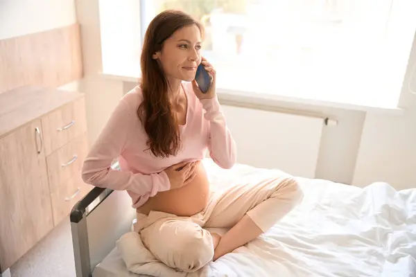 有魅力的快乐孕妇在产前护理中心用智能手机打电话 — 图库照片