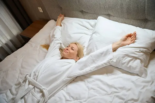 Contented Lady Bathrobe Lying Supine Bed Bedroom Doing Arm Stretch — Stock Photo, Image