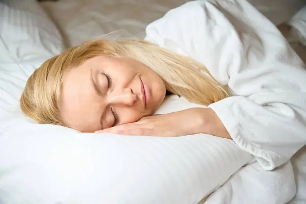 ベッドの白い枕に閉じられた目で横たわるテリーバスローブの穏やかな女性 — ストック写真