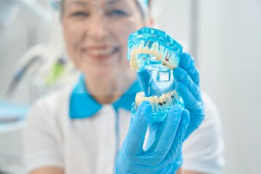 Kameraya farklı diş enfeksiyonları ve hastalıkları olan ve önleme ve tedavi yöntemini açıklayan şeffaf üç boyutlu çene modelini gösteren kadın diş asistanı