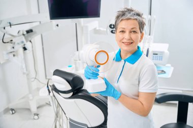 Üniformalı gülümseyen diş asistanı ve portatif diş röntgeni cihazı tutan koruyucu lastik eldivenler, diş ve diş etlerini iltihaplanma varlığında incelemeye yardımcı oluyor.