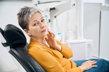 Worried mature woman sitting in dental examination chair, suffering toothache and filling pain, emergency appointment and urgency treatment, aesthetic dentistry clinic clipart