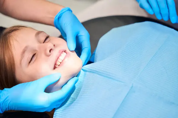 stock image Smiling girl is placed in a chair for dental procedures, the medical staff works in protective gloves