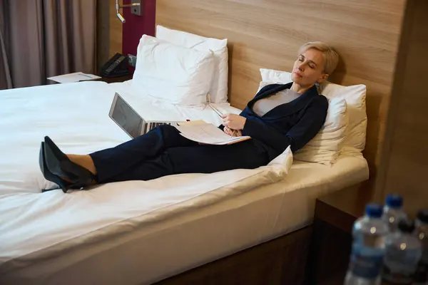 Adult caucasian businesswoman sleeping on bed during work in hotel room at daytime. Concept of business trip, vacation and travelling