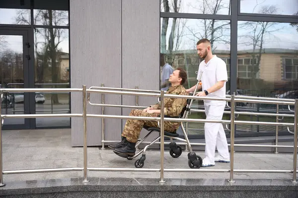 Seitenansicht Eines Arztes Der Rollstuhl Mit Servicekräften Richtung Krankenhaustür Schiebt Stockbild