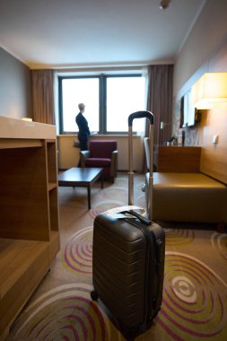 Gündüz vakti otel odasının penceresinden bakan ve ayakta duran iş kadınının bulanık geçmişine sahip bavulun ön planına odaklan. İş gezisi, tatil ve seyahat kavramı