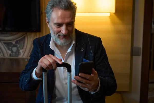 Erwachsener Kaukasischer Geschäftsmann Mit Koffer Und Smartphone Verschwommenen Hotelzimmer Tagsüber lizenzfreie Stockfotos