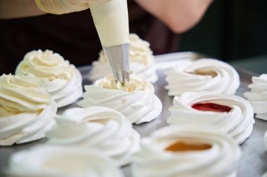 Şekerci krema torbasından krem şantili krema sıkıyor. İçinde meyveli süt var. Mini pavlova tatlı hazırlıyor.