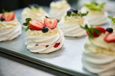 Yakın çekim ışık, çıtır çıtır ve havadar kremalı ve kremalı krema ve taze meyveli mini Pavlova tatlısıyla dolu kremalı krema yuvaları.