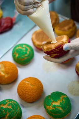 Yakın plan kadın fırıncı choux au craquelin 'i yoğunlaştırılmış süt, karamel kreması veya muhallebi ile dolduruyor, tatlı ve lezzetli bir tatlı hazırlıyor.