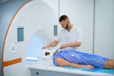 Hasta MRI masasında sırtüstü yatarken, teknoloji uzmanları kafasının etrafına bobin yerleştiriyor.