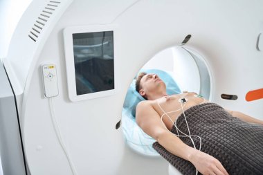 Göğüs kafesinde ECG elektrotları olan yetişkin bir erkek. Tomografi boşluğunda sırtüstü yatıyor.