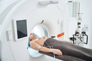 Göğsüne ECG elektrotları bağlanmış bir adam bilgisayarlı tomografi açıklığında sırtüstü yatıyor.