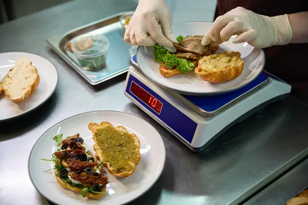 女厨师将莴苣叶和冷猪肉片加入切碎的烤牛角面包中 配上辛辣的红辣椒酱 羊角三明治 — 图库照片