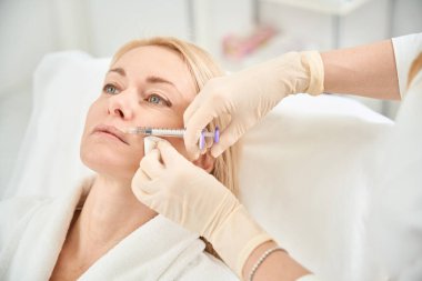 Yakın plan nitelikli güzellik uzmanı, dolgu malzemesi kullanarak kadın müşteri dudaklarının şeklini ve boyutunu düzeltiyor, hücre ve dudak dokularının yenilenmesi, estetik tıp kliniği.