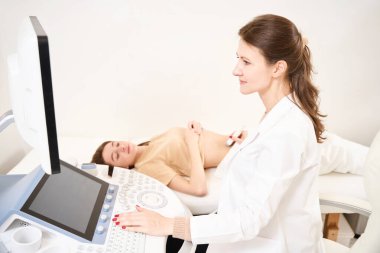 Kafkasyalı kadın jinekolog, klinikte doktora bakan Avrupalı genç bir kadının hamile karnının ultrason taramasını yapıyor. Hamilelik ve annelik kavramı