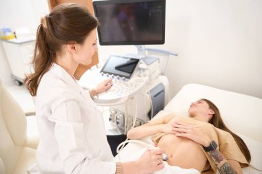 Yetişkin kadın jinekolog, klinikte genç bir kadının karnının ultrason taramasını yapıyor. Hamilelik ve annelik kavramı