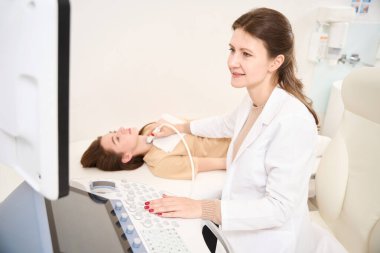 Gülümseyen beyaz kadın doktor klinikte tiroid bezini ultrasonla tarıyor. Sağlık hizmetleri kavramı