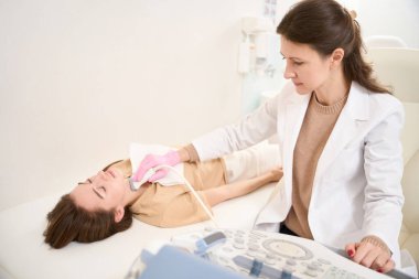 Kafkasyalı kadın doktor hastanede gözleri kapalı genç bir kadının tiroid bezini ultrason taraması yapıyor. Sağlık hizmetleri kavramı