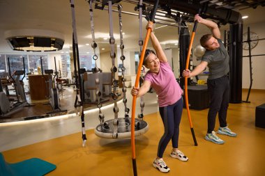 Erkek antrenör ve orta yaşlı gülümseyen beyaz kadın spor kıyafetleri giyiyor spor salonunda spor sopalarıyla spor yapıyor. Modern sağlıklı yaşam tarzı kavramı