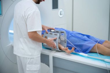 Hastanın MRI masasında yatarken çekilmiş bir fotoğrafı. Bu sırada sağlık uzmanları kolunun etrafına ekstremite bobini yerleştiriyor.
