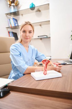 Kafkas kadın jinekolog, klinikte çalışırken masada oturup kameraya bakıyor. Sağlık hizmetleri kavramı