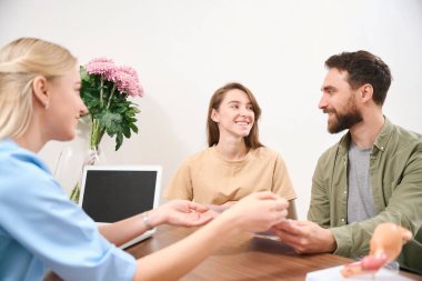 Kafkasyalı kadın jinekolog, klinikte danışmanlık yaparken birbirlerine bakan genç Avrupalı bir çifte ikizlerle hamile karnının ultrason taramasını gösteriyor. Hamilelik ve babalık