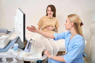 Kafkasyalı kadın jinekolog, klinikteki gülümseyen Avrupalı genç hamile kadına ultrason taraması sonucu ortaya çıktı. Hamilelik ve annelik kavramı