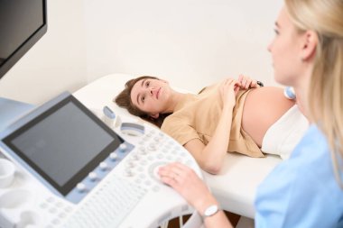 Kısmi bulanık kadın jinekolog klinikte genç Avrupalı bir kadının hamile karnını ultrasonla tarıyor. Hamilelik ve annelik kavramı