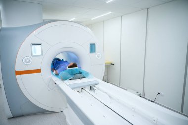 Gürültü önleyici kulaklıklar takan hasta ve dizine sargılar yerleştirilmiş ve MRI tarayıcısının içindeki masada sırtüstü yatıyor.