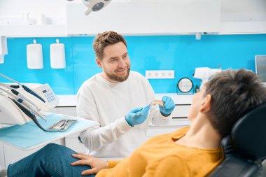 Olumlu diş hekimi üst çene modeli tutuyor ve orak prob ile yetişkin kadın istemciye sorun bölgesi gösteriyor