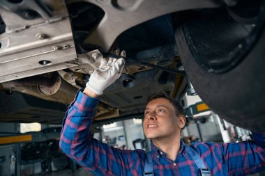 Koruyucu eldivenli genç erkek, araç hizmet merkezinde makine süspansiyonunu tamir etmek için araç kullanıyor.