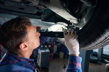 Koruyucu eldivenli bir erkek fener tutuyor ve fren sisteminde bakım yapıyor.