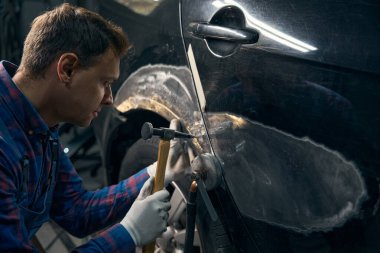 Otomobilin yanında duran, elinde çekiç tutan ve boyayı çıkaran profesyonel erkek, metali işliyor.