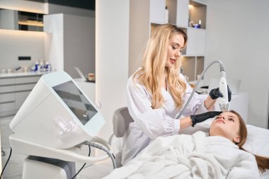 Avrupalı kadın kozmetik uzmanı, güzellik salonunda genç beyaz bir kadının IPL fotorejuvenizasyon cihazıyla kafa derisini mikronedle kaldırıyor. Yüz bakımı ve gençleştirme kavramı