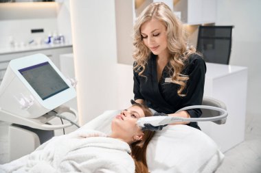 Bulanık güzellik salonunda genç beyaz bir kadının IPL fotorejuvenation cihazıyla yüz derisini mikronedle kaldırıyor. Yüz bakımı ve gençleştirme kavramı