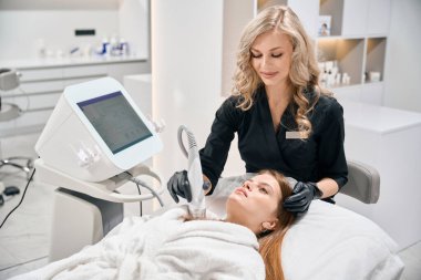 Bulanık güzellik salonunda genç beyaz bir kadının IPL fotorejuvenation cihazıyla göğüs derisinin mikronedle kaldırılmasını yapan Avrupalı kadın güzellik uzmanı. Vücut bakımı ve gençleştirme kavramı